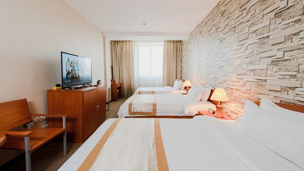 A hotel room with two beds, a TV, a wooden desk, and a stone wall.