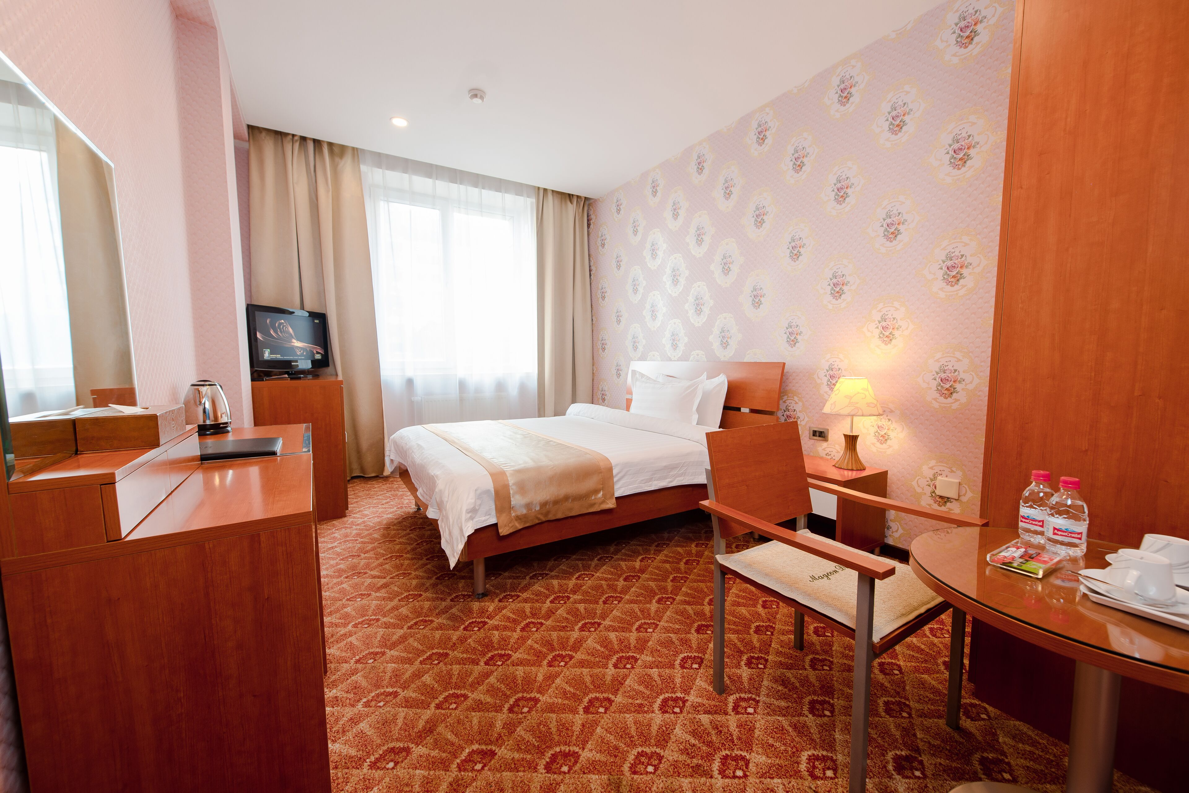 Una habitación de hotel con cama, escritorio, silla, televisor y lámpara.