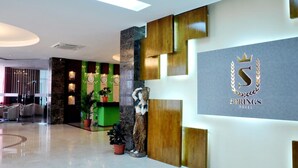 A modern hotel lobby with a reception desk, a statue, and a logo on the wall.
