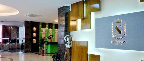 A modern hotel lobby with a reception desk, a statue, and a logo on the wall.