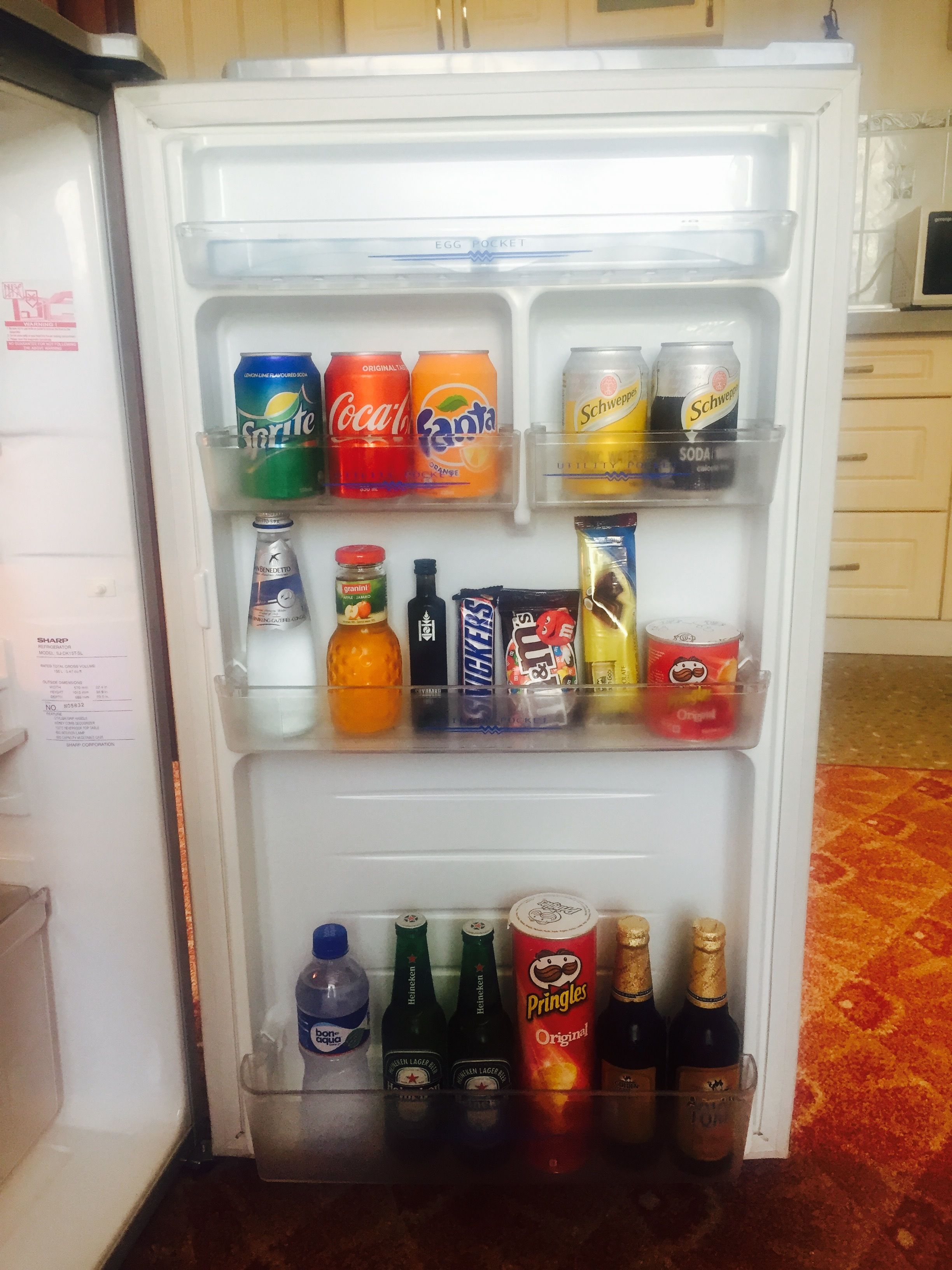 Un refrigerador lleno de diversas bebidas, como latas de refresco, botellas y aperitivos.