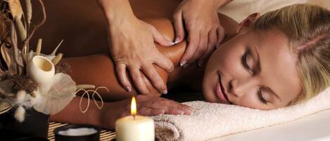 En person får massage med hjälp av ett ljus och en liten skål, och ligger på en matta.