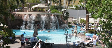 Un espace piscine agrémenté d’une cascade, de chaises longues et de palmiers.