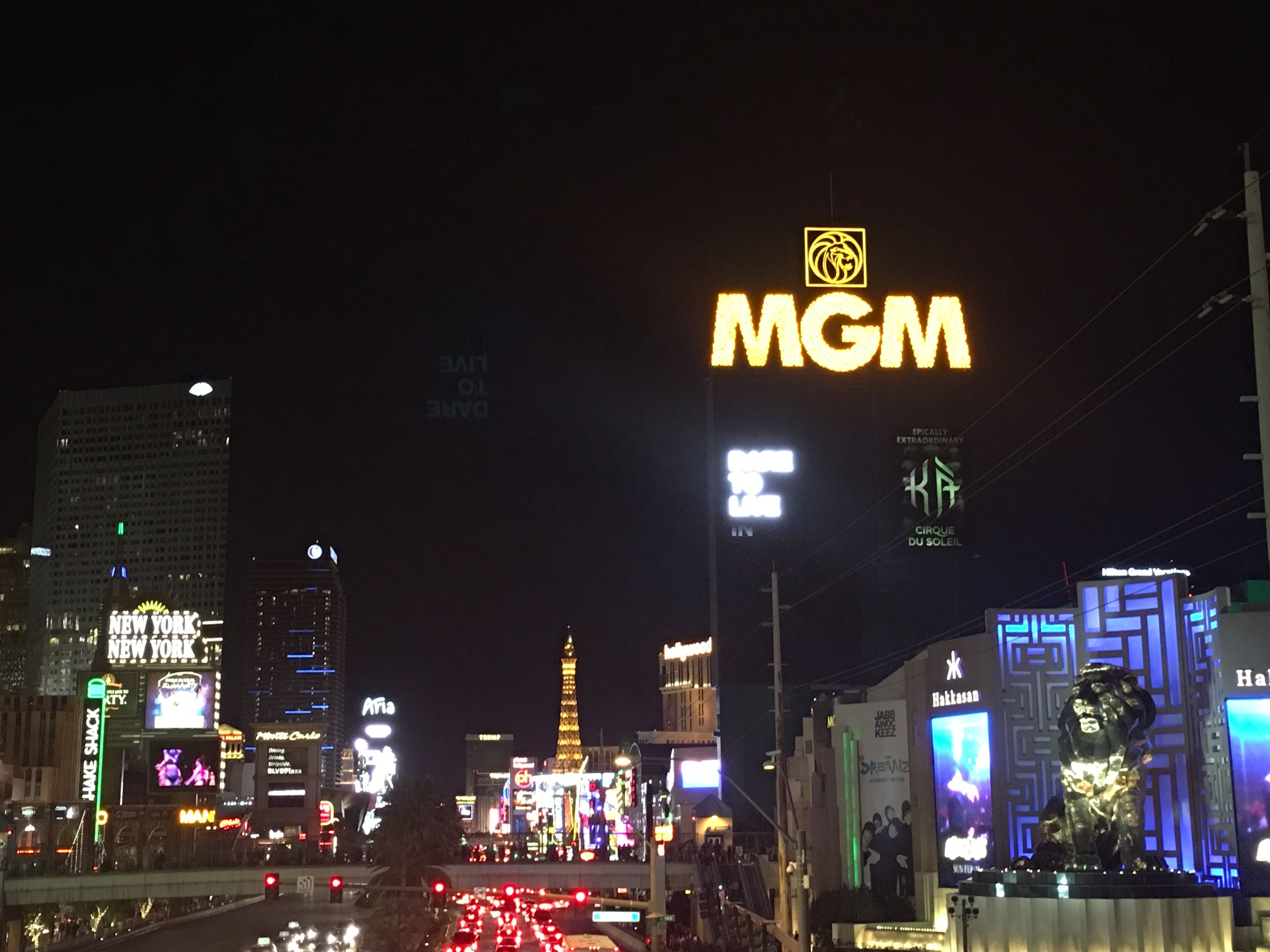 Une vue nocturne d’une ville, avec de nombreux panneaux lumineux bien visibles, notamment un grand panneau « MGM » et diverses autres publicités commerciales.