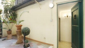 Un pasillo con una puerta verde, plantas en macetas y suelo de baldosas.