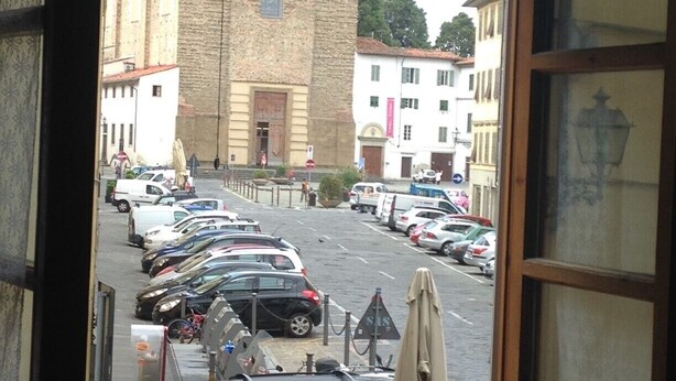 Vista desde una ventana que da a una calle con coches aparcados y un edificio histórico con fachada de piedra.