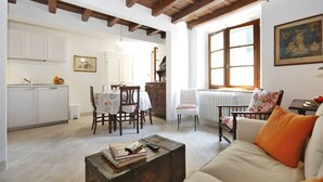 Amplia sala de estar con mesa de comedor, sillas, sofá y una mesa de centro. Cuenta con una zona de cocina con armarios y un radiador.