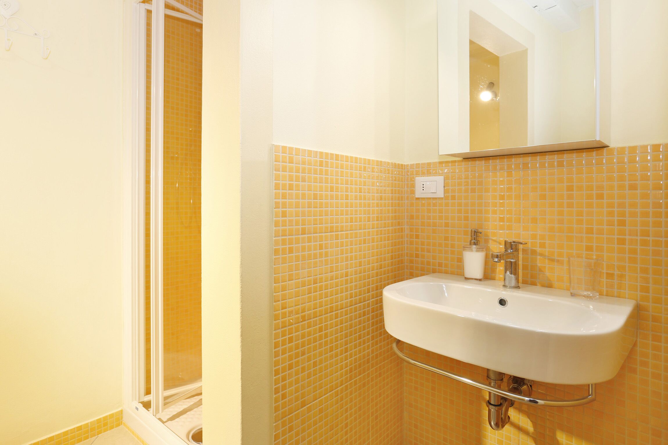 A bathroom with a white sink, yellow-tiled walls, and a glass shower enclosure.
