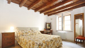 Un dormitorio con techo de madera, una cama con ropa de cama floral, una mesita de noche, un aparador, un espejo y una ventana con vistas.