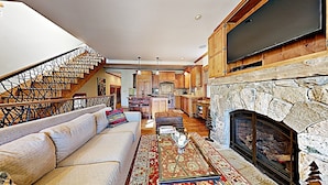 A spacious living room with a stone fireplace, a large TV mounted above it, and a cozy seating area with a sofa and ottoman.