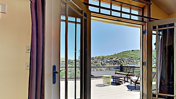 An open sliding glass door leading to an outdoor patio with a view of a hillside town.