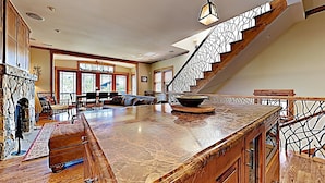 A spacious kitchen with a large island, a stone fireplace, and a staircase with a decorative railing.