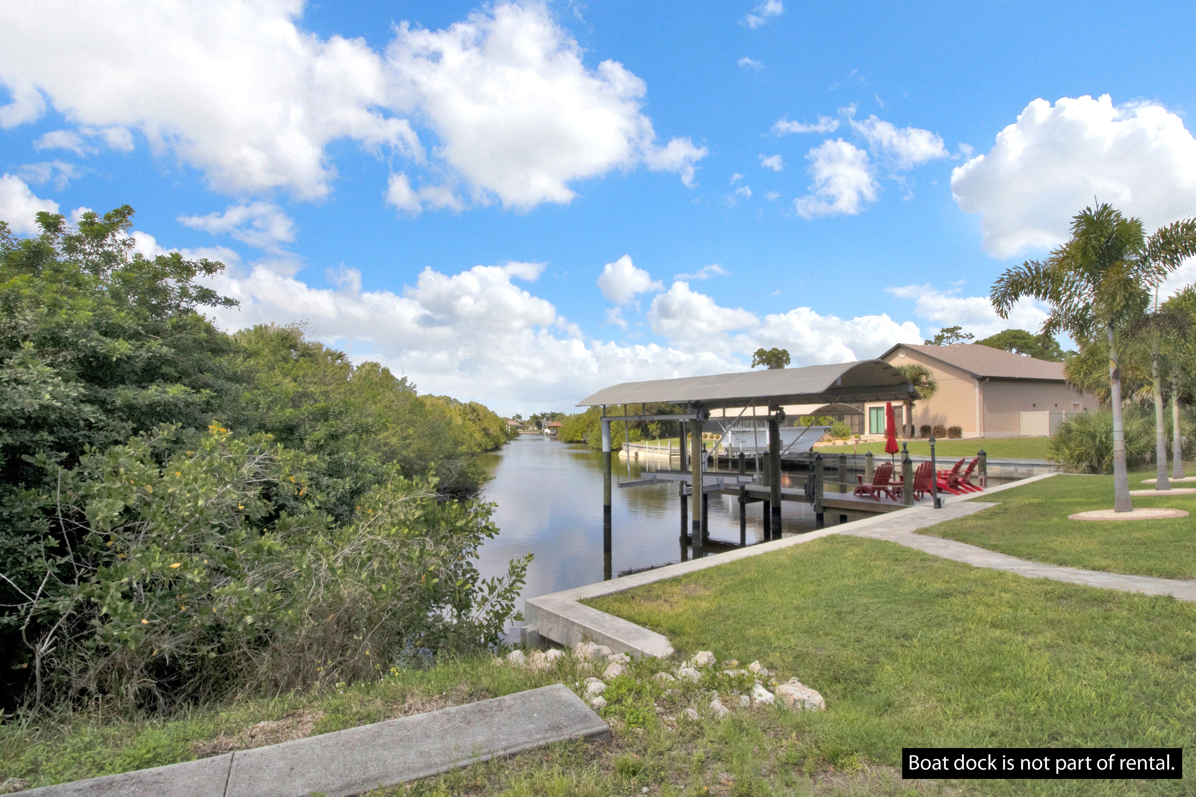 A boat dock and a covered area with chairs and a table, with a river and greenery in the background.