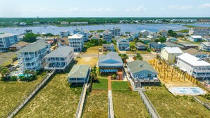 An aerial view of a coastal residential area with multiple two-story houses, some with balconies, and a marina with boats in the background.