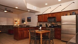 Una cocina con armarios de madera, microondas, refrigerador, una mesa de comedor con sillas y un ventilador de techo.