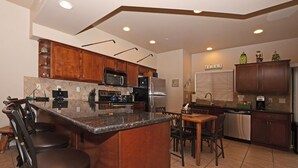 Una cocina moderna con armarios de madera, una isla central con taburetes, electrodomésticos de acero inoxidable y un comedor con mesa y sillas.