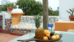 Een betegeld buitenzitgedeelte met een fruitschaal met een ananas, appels en sinaasappels.