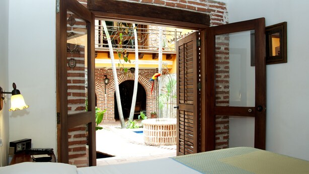Een open deuropening die uitkomt op een binnenplaats met een bakstenen boog, een hangplant en een kleine tafel.