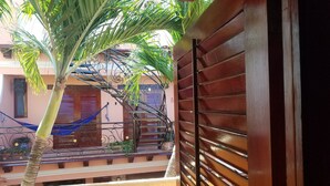 Een balkon met houten hekwerk, een hangmat en een trap naar een hoger niveau.