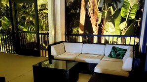 A modern living room with a sectional sofa, a glass coffee table, and a view of tropical plants through a glass door. - IMPERIAL PARADISE Naples, SFH, HEATED/CAGE pool, Near Beaches, discounts avail (Bonita Springs)