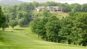 A golf course with a clubhouse in the background surrounded by dense trees.