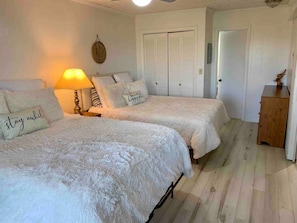 Ein Schlafzimmer mit zwei Betten, einem Nachttisch mit Lampe, einer Holzkommode und einem Kleiderschrank mit Klappläden.
