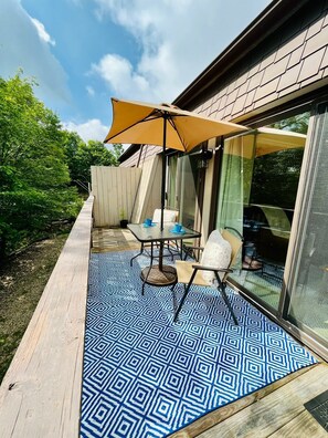 A patio with a patterned floor, a table with chairs, and a large umbrella. - All You Need! Land of Oz + Concerts + Pets! (Beech Mountain)
