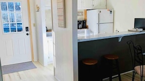 A kitchen with white cabinets, a refrigerator, a coffee maker, and a bar stool.