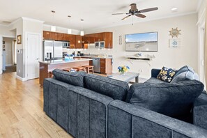 A modern kitchen with wooden cabinets, a central island, and a dining area with a gray sofa and a table.