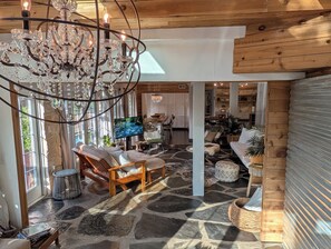 A spacious living area with a stone floor, wooden furniture, a large chandelier, and a television. - KAYAK-SUP-SWIM--ALL YEAR, Gorgeous  LAKE walks-Just STEPS away & Restaurants (Austin)