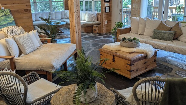 Een knus interieur van een chalet met een stenen vloer, houten meubels en grote ramen met uitzicht op het landschap.