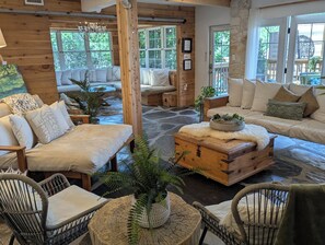 A cozy cabin interior with a stone floor, wooden furniture, and large windows offering views of the outdoors. - KAYAK-SUP-SWIM--ALL YEAR, Gorgeous  LAKE walks-Just STEPS away & Restaurants (Austin)