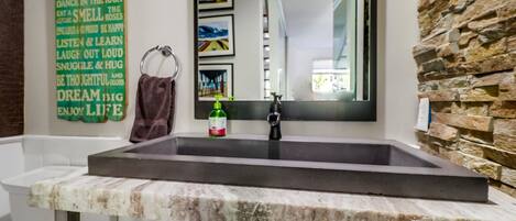 A bathroom with a marble sink, a stone wall, a framed motivational quote, and a mirror reflecting a room with a window.