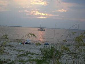A beach with a sailboat in the distance, a tent, and some beach chairs.
