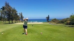 Un parcours de golf offrant une vue dégagée sur l’océan et un sentier menant à la plage.
