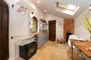 A modern kitchen with a built-in oven, a wooden dining table, and a brick fireplace. - Bothy In Victorian Walled Garden (Worcester)