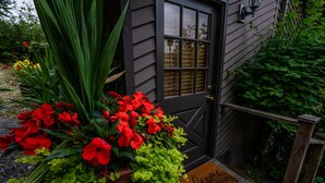 A dark wooden door with a window, surrounded by lush greenery and vibrant red flowers. - Private Cottage and Hot Tub, Spectacular Sunset & Mtn Views (Burien)