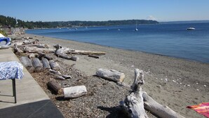 A beach with driftwood and a table with a blue tablecloth. - Private Cottage and Hot Tub, Spectacular Sunset & Mtn Views (Burien)