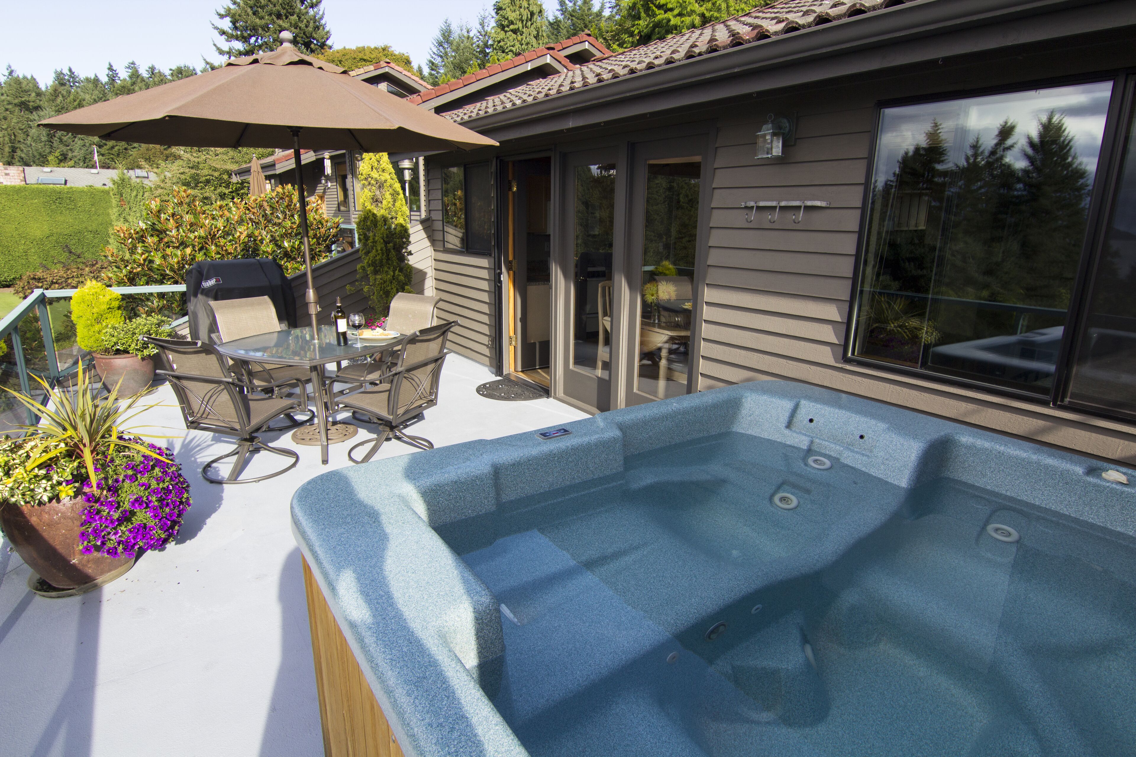 Jacuzzi en un patio con mesa y sillas, una planta en maceta y un ventanal corredera.