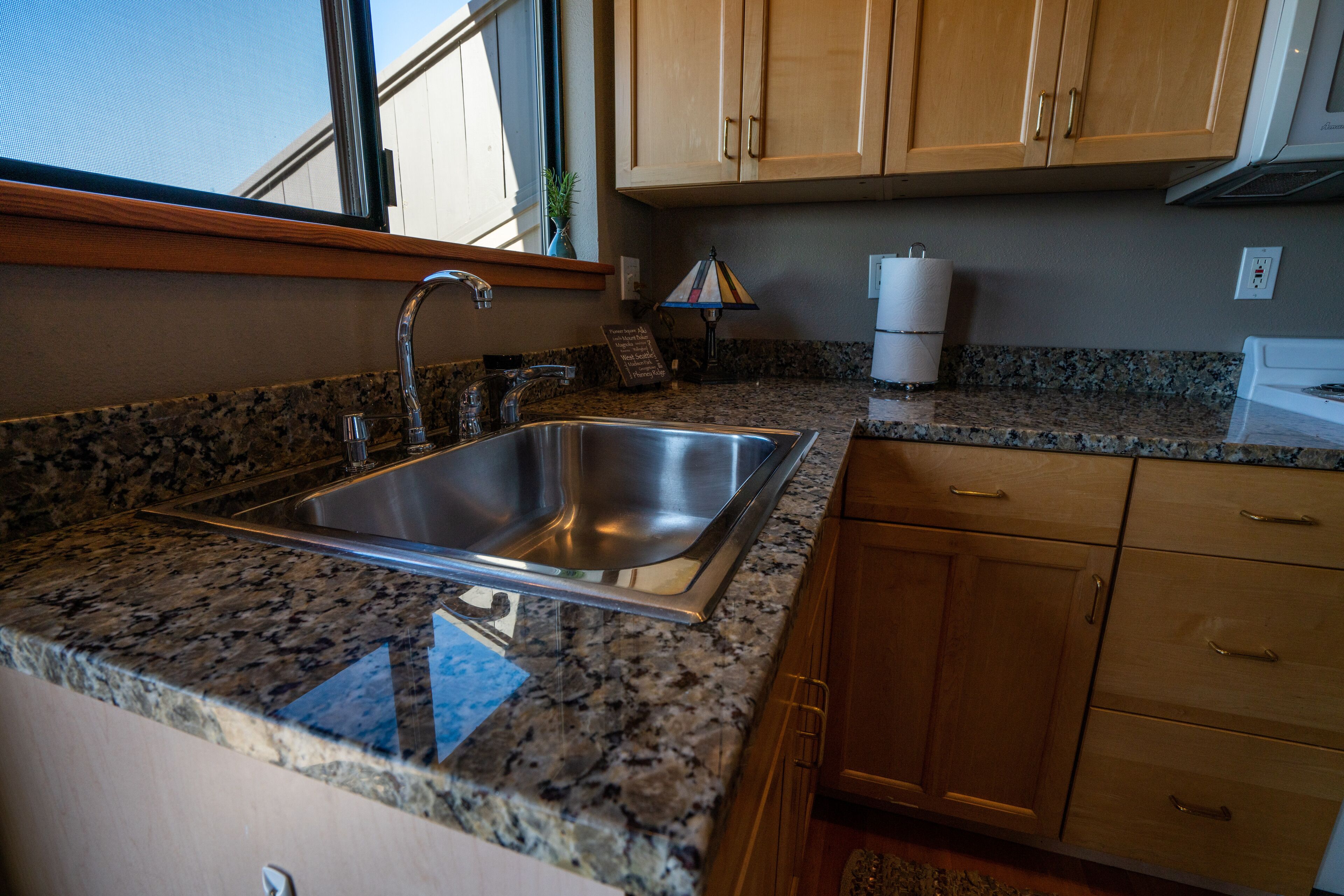 A kitchen with granite countertops, stainless steel sink, wooden cabinets, and a window above the sink.