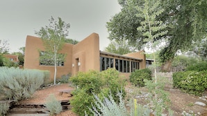 Un edificio moderno con facciata intonacata, circondato da un giardino curato con arbusti diversi e una scala in legno che conduce all'ingresso.