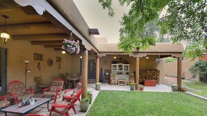Un patio con sedie rosse, un tavolo, cesti di fiori pensili e una zona coperta con un camino.