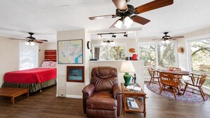 A spacious living room with a large brown leather sofa, a dining area with wooden chairs, and a ceiling fan. - Peaceful Farm Cabin for Couples | TX Hill Country (Georgetown)