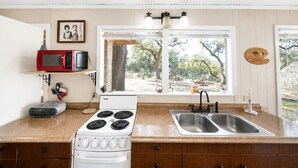 A kitchen with a stove, microwave, and double sink. - Peaceful Farm Cabin for Couples | TX Hill Country (Georgetown)
