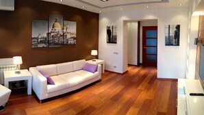 A modern living room with a white sofa, a side table with a lamp, and a wooden floor.
