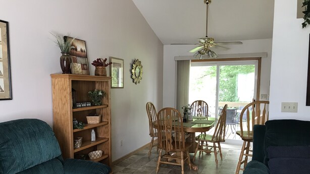 Ein Wohnzimmer mit einem dunkelgrünen Sofa, Holzstühlen, einem Esstisch und einem Deckenventilator.