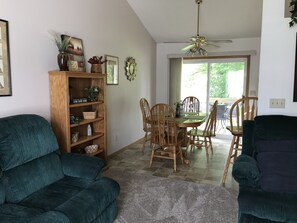 Ein Wohnzimmer mit einem dunkelgrünen Sofa, Holzstühlen, einem Esstisch und einem Deckenventilator.