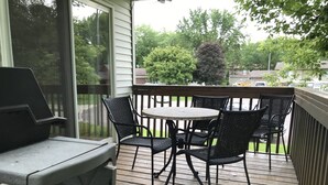 Eine überdachte Terrasse im Freien mit Tisch, Stühlen, einem Grill und Blick auf die Nachbarschaft.