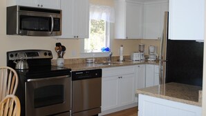 A kitchen with white cabinets, stainless steel appliances, a window with a white valance, and a countertop with various items. - Ocean Cottage A/C near PB and Beachcomber. Steps to the beach! (Wellfleet)