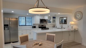 Une cuisine moderne avec des meubles blancs, un îlot central et un coin repas comprenant une table ronde et des chaises.
